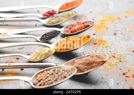 Cucchiai con spezie diverse su sfondo grigio Foto Stock