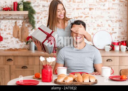 Felice giovane donna che dà regalo di Natale al suo ragazzo a casa Foto Stock