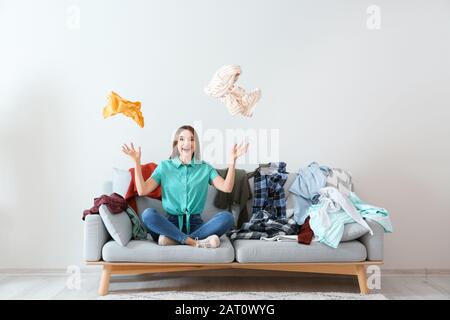 Giovane donna con mucchio di vestiti sul divano interno Foto Stock