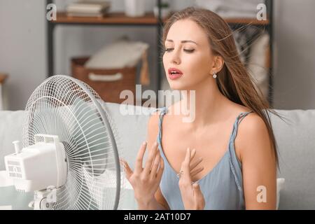 Giovane donna che usa il ventilatore elettrico durante l'onda di calore a casa Foto Stock