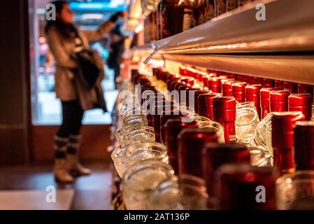 Vista prospettica di un barchotto di una donna che fa shopping per vino o altro alcool in un negozio di liquori che si trova davanti a scaffali pieni di bottiglie. Foto Stock