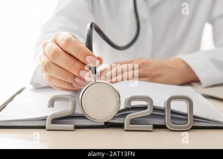 Medico femminile con stetoscopio, notebook e figura 2020 sul tavolo, closeup Foto Stock