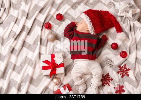 Carino piccolo bambino in cappello di Babbo Natale e con regali di Natale dormire su plaid, vista dall'alto Foto Stock