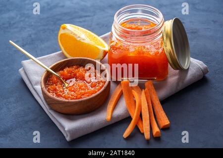 Marmellata di carote in un vaso e una ciotola di legno su uno sfondo scuro. Orientamento orizzontale Foto Stock