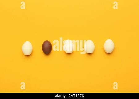 Cioccolato marrone uovo di Pasqua tra quelli bianchi su sfondo colorato. Concetto di unicità Foto Stock