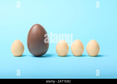 Cioccolato marrone uovo di Pasqua tra quelli bianchi su sfondo colorato. Concetto di unicità Foto Stock