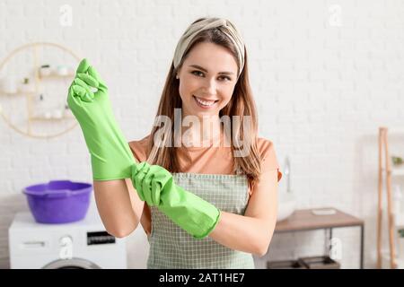 Giovane casalinga che mette su guanti di gomma prima di pulire piatto Foto Stock