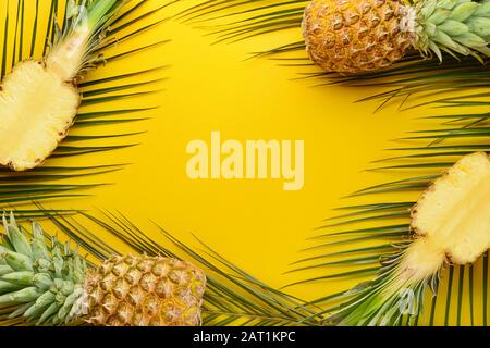 Ananas freschi maturi e foglie tropicali su sfondo colorato Foto Stock