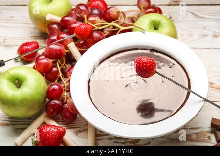 Immersione di gustose fragole in un recipiente con la fonduta di cioccolato su tavola Foto Stock