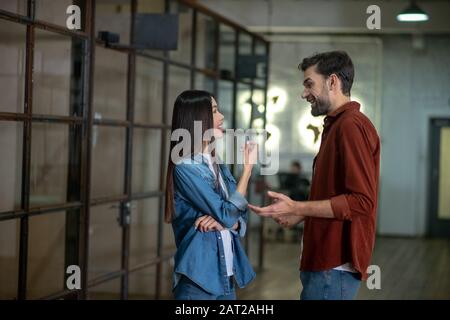 Bell'uomo bearded in una camicia marrone che discute qualcosa con il suo collega femminile Foto Stock