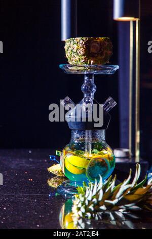 Produzione di zoccoli nell'ananas. L'ananas tagliato si trova nella ciotola della narghilè. Fiasca rotonda con cappuccio e liquido blu. Hookah sull'ananas. Foto Stock