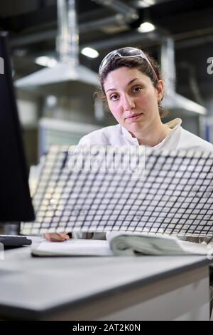 Donna in camice bianco con rete in carbonio si siede sul tavolo in laboratorio, sfondo sfocato Foto Stock