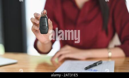 Scatto corto di ragazza di fiducia giovane sorridente e che mostra la chiave mentre sedendosi alla scrivania nell'ufficio moderno. Foto Stock