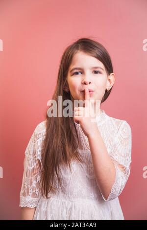 una bella ragazza in un abito bianco pone in modo giocoso su uno sfondo rosa Foto Stock