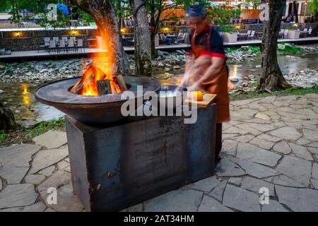 Barbecue con un fuoco acceso sulla riva del fiume di montagna la sera. Accanto alla griglia verdure preparate per friggere: Peperoni, pomodori, mu Foto Stock