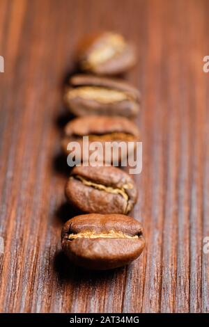 Disposti in una fila di chicchi di caffè su uno sfondo di legno bruciato. Verticale. Primo piano. Foto Stock