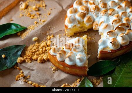 Tartlet Al Limone Con Crema Di Lime O Curd E Meringa Italiana Su Carta Artigianale. Taglio Di Una Sezione Tartlet. Concetto Di Pasticceria Fatta In Casa E Des Foto Stock