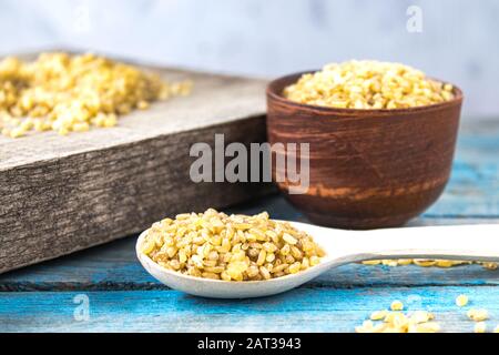 Grano di bulgur asciutto in un cucchiaio di legno. Prodotto sano, dietetico, vegano, senza glutine. Foto Stock