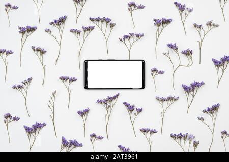 Su uno sfondo bianco ci sono fiori selvatici e uno smartphone con uno schermo vuoto. Posiziona per testo, Foto Stock