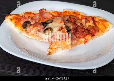 fetta di pizza con formaggio bacon e olive si trova su un piatto Foto Stock