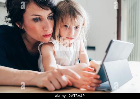 Madre e figlia indoor utilizzando tablet - learning, intrattenimento, concetto di insegnamento Foto Stock