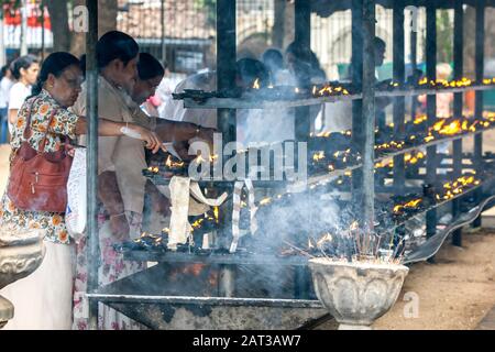 I pellegrini buddisti illuminano le lampade ad olio all'interno del Tempio del complesso della Reliquia Dei Denti Sacri a Kandy in Sri Lanka. Foto Stock