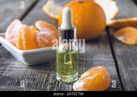 Olio essenziale di mandarino in una bottiglia di vetro vicino a una ciotola bianca con fette di mandarino. Agrumi, tangerini o arance. Medicina alternativa Foto Stock