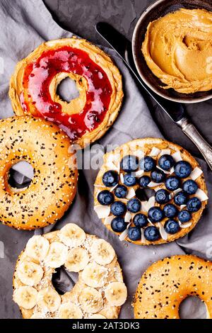 Varietà di bagel con diversi condimenti e noce paleo naturale arachidi burro cremoso su sfondo grigio scuro primo piano. Sana colazione brunch Foto Stock