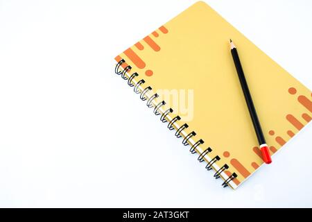 Una matita nera scura su un notebook dal design arancione con uno sfondo bianco isolato. Foto Stock