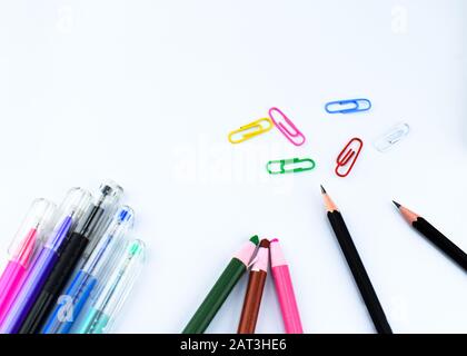 materiali didattici disposti su uno sfondo bianco che include cinque penne, due matite nere, tre pastelli e alcune graffette. Foto Stock