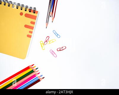 Materiali di studio sparsi su una tabella bianca, che contiene un taccuino, tre matite, sei pastelli e alcune graffette. Foto Stock