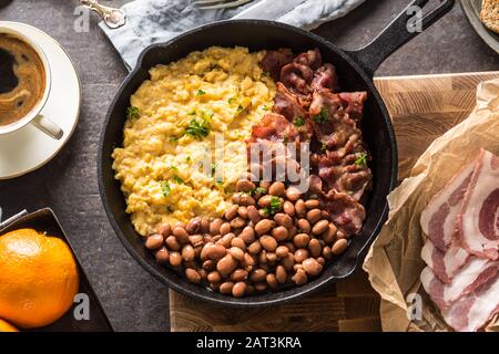 Tavolo completo con colazione all'inglese. Uova strapazzate pancetta fagioli grigliati pane tostato succo d'arancia e caffè Foto Stock