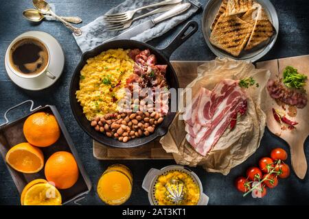 Tavolo completo con colazione all'inglese. Uova strapazzate pancetta fagioli grigliati pane tostato succo d'arancia e caffè Foto Stock