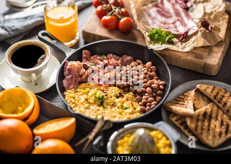 Tavolo completo con colazione all'inglese. Uova strapazzate pancetta fagioli grigliati pane tostato succo d'arancia e caffè Foto Stock