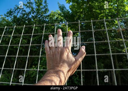 Una mano appoggia contro una rete metallica Foto Stock