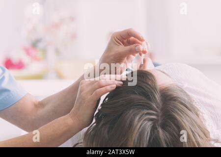 Terapista di agopuntura applicando aghi di agopuntura per la sua testa della cliente Foto Stock