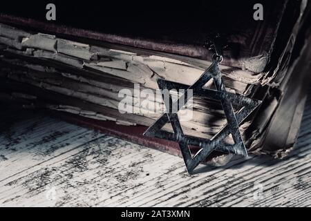 primo piano di un vecchio pendente arrugginito a forma di stella di davide accanto ad un vecchio libro, su una superficie rustica in legno, con una luce drammatica Foto Stock