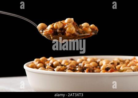 primo piano di forchetta e piatto con uno stufato di ceci vegetariano con alghe kombu, su una superficie grigia rustica, su sfondo nero Foto Stock