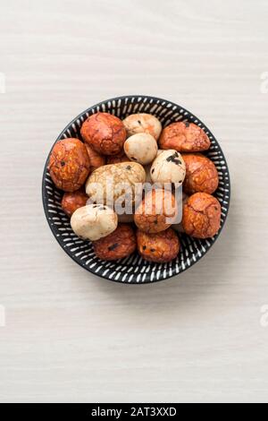 vista ad alto angolo di una pila di snack orientali in un recipiente bianco e nero, su una superficie di legno bianco Foto Stock