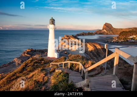 Vista panoramica sulle scogliere di Castlepoint, il faro e la laguna dalle scale durante il tramonto con cielo blu. Isola Del Nord, Nuova Zelanda Foto Stock