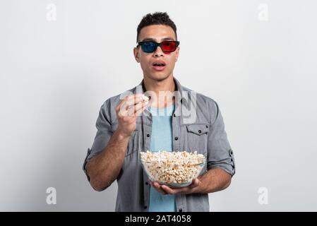 L'uomo negli occhiali 3D si alza con un piatto di popcorn nelle sue mani e guardando si aprì la bocca si divertì Foto Stock