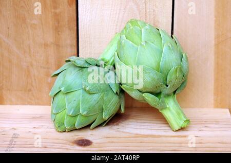Due carciofi freschi su tavola di legno al mercato Foto Stock