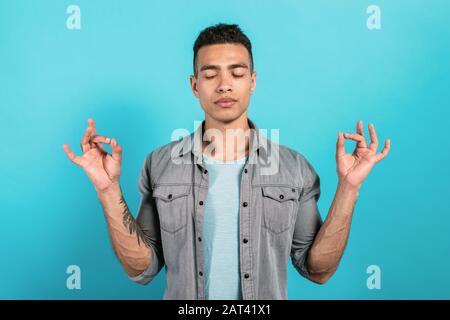 L'uomo medita mentre si trova in piedi su uno sfondo blu, chiudendo gli occhi e tenere le braccia in yoga-mudra Foto Stock