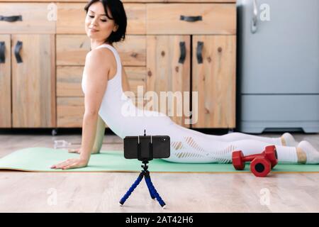 Attraente giovane donna di fitness che indossa abbigliamento sportivo facendo esercizi di stretching, utilizzando tappetino fitness Foto Stock