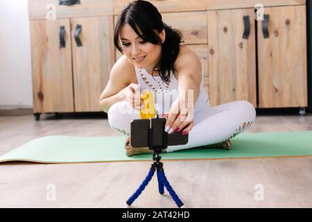 Giovane donna che indossa lo sportswear bianco che fa yoga mentre si siede in posizione lotus, spara video Foto Stock