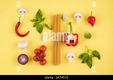Cucina italiana. Su sfondo giallo, una serie di ingredienti, pasta, pomodori, peperoni, funghi, basilico Foto Stock