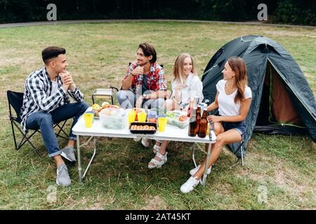 Ragazzi seduti al tavolo durante il pranzo in campeggio e parlare Foto Stock