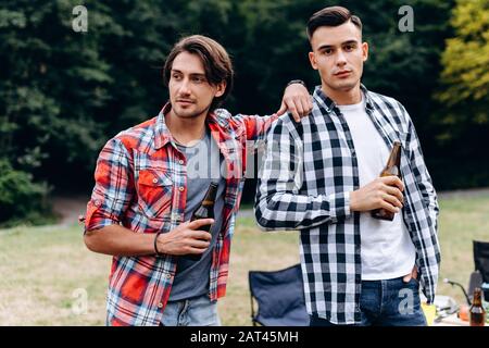 Due ragazzi in piedi e con una birra in campeggio. - Immagine Foto Stock