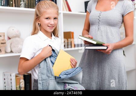 Cute, ragazza attraente mette i libri in una borsa, la sua madre la aiuta. Preparandosi per la scuola Foto Stock