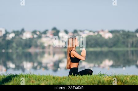 Donna seduta in meditazione posa all'aperto con il gesto namaste dalle sue mani. Vista laterale- immagine Foto Stock